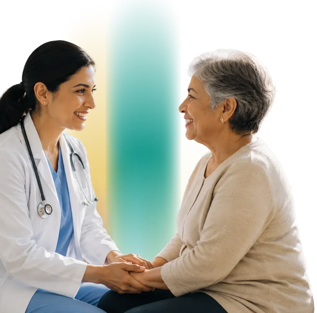 A physician holds an older patient’s hands and smiles with her