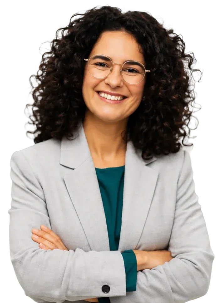 A smiling business leader with curly hair and glasses stands with arms crossed
